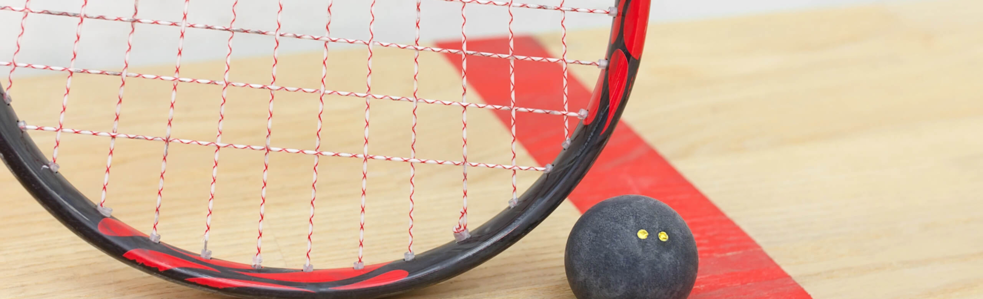 A squash racket rests beside a black squash ball on a wooden surface.