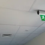 A ceiling with an emergency exit sign and a ventilation grille visible.